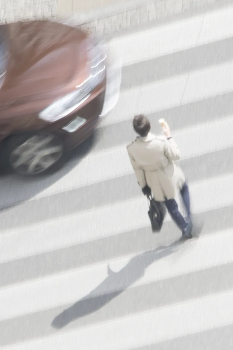 Person in a long trench coat crossing a zebra crossing while holding up a phone